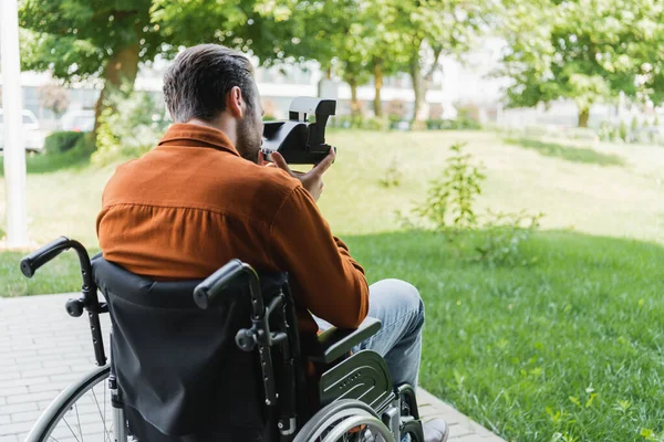 Vista posteriore di uomo handicappato in sedia a rotelle scattare foto sulla fotocamera vintage all'aperto — Foto stock