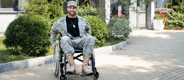 Інвалідний військовий у інвалідному кріслі посміхається на камеру на відкритому повітрі, банер — стокове фото