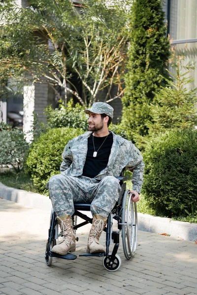 Handicapé militaire en fauteuil roulant souriant tout en regardant loin à l'extérieur — Photo de stock