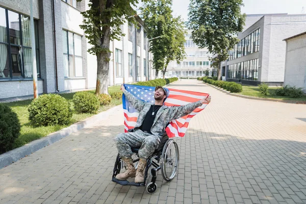 Überglücklicher gehandicapter Soldat im Rollstuhl hält US-Fahne in der Hand und lacht auf der Straße — Stockfoto
