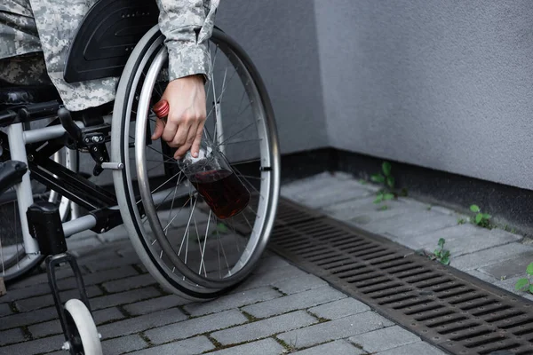 Vue partielle de l'homme militaire handicapé avec bouteille de whisky assis en fauteuil roulant à l'extérieur — Photo de stock