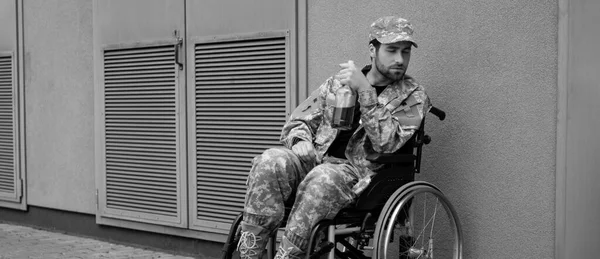 Молодий інвалідний солдат сидить у інвалідному кріслі з пляшкою алкоголю на відкритому повітрі, банер — стокове фото