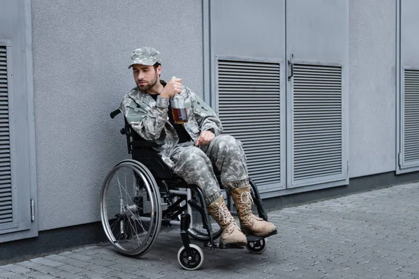 Handicapped veteran sitting in wheelchair with bottle of alcohol on city street — Stock Photo