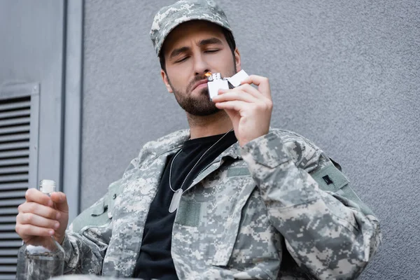Handicapped military man with bottle of alcohol lighting cigarette outdoors — Stock Photo
