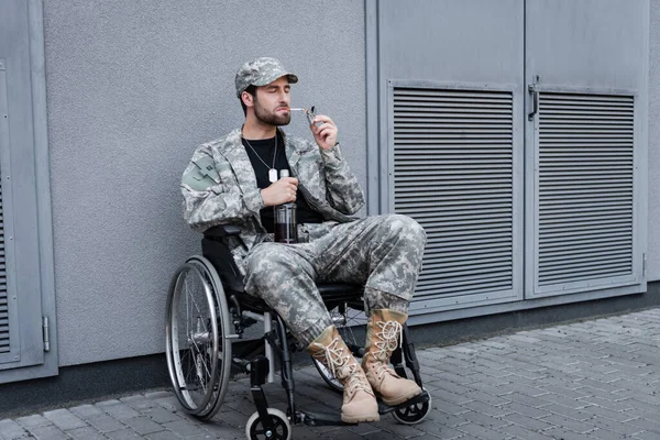 Behinderter Veteran im Rollstuhl zündet sich Zigarette an und hält Flasche Alkohol im Freien — Stockfoto