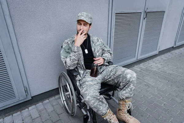 Vue grand angle de vétéran handicapé avec bouteille de whisky fumeur en fauteuil roulant à l'extérieur — Photo de stock