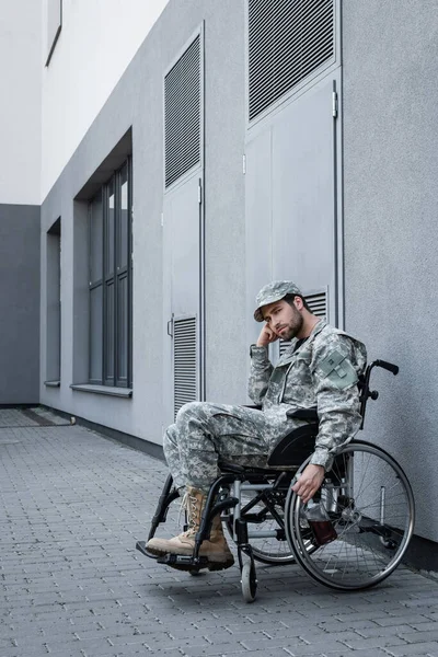 Disabled military man in wheelchair holding bottle of whiskey near grey building outdoors — Stock Photo