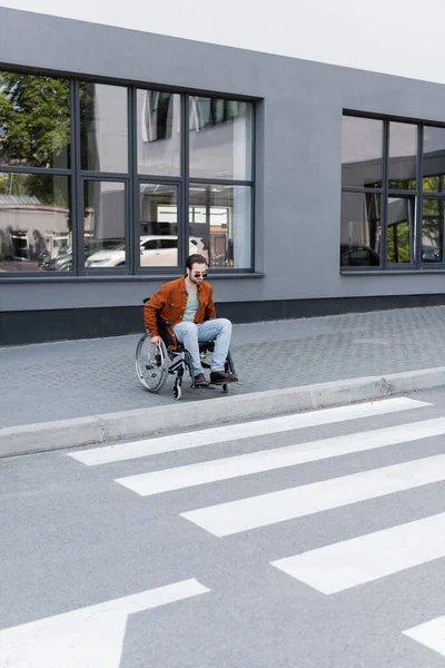 Jovem deficiente homem em cadeira de rodas perto de passarela com fronteira na cidade — Fotografia de Stock