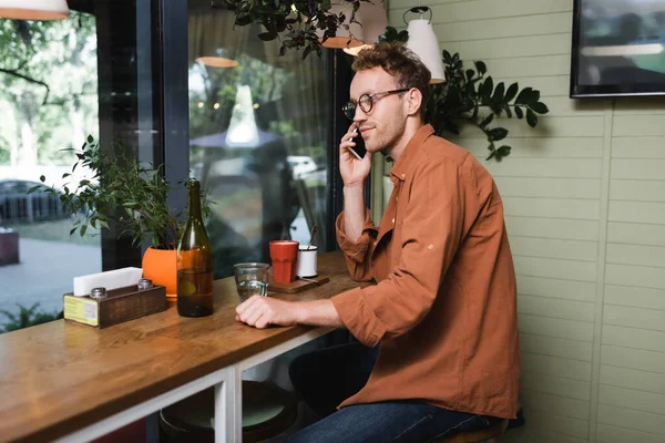 Junger Mann mit Brille spricht im Café auf Smartphone — Stockfoto