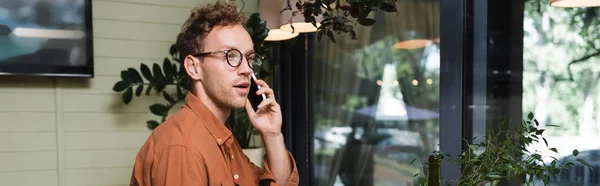 Joven en gafas hablando en el teléfono inteligente en la cafetería, pancarta - foto de stock