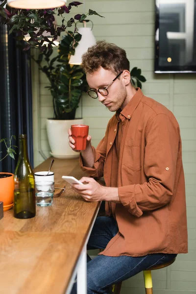 Giovane uomo in occhiali che scrive su smartphone in caffè — Foto stock