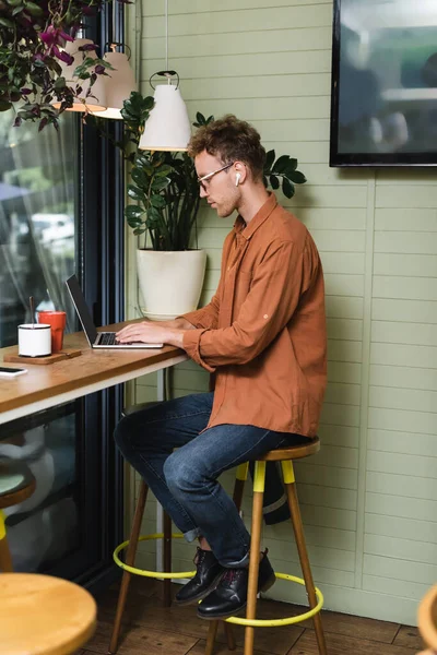 Vista lateral del joven en gafas de escribir en el ordenador portátil en la cafetería - foto de stock