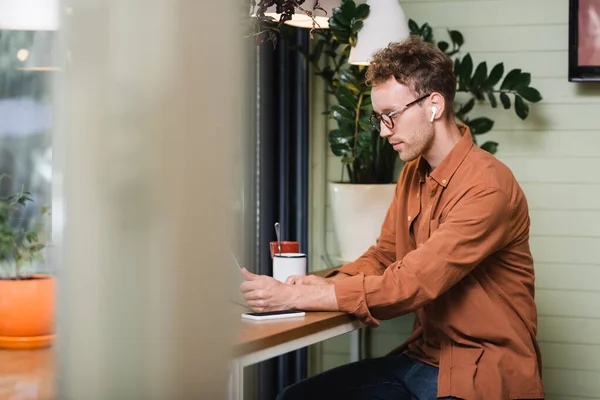 Libero professionista in occhiali che guardano il computer portatile vicino a smartphone in caffè — Foto stock