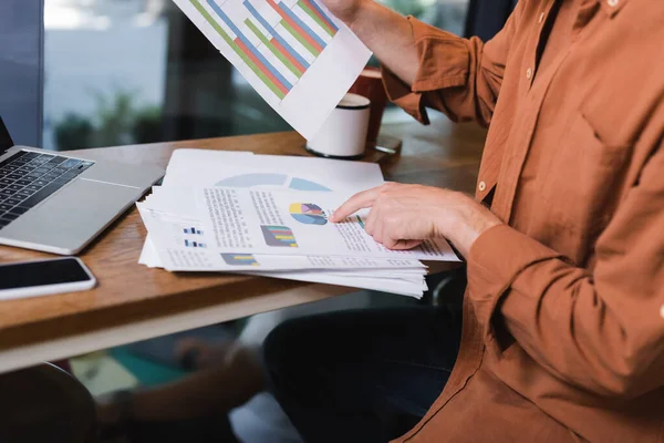 Cropped view of young man pointing at graphs near gadgets in cafe — Stock Photo