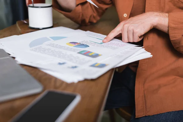 Vista ritagliata di giovane uomo che punta a grafici e grafici vicino gadget in caffè — Foto stock