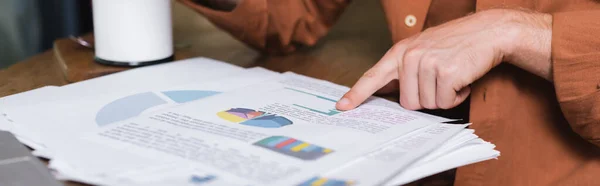 Cropped view of young man pointing at charts and graphs in cafe, banner — Stock Photo