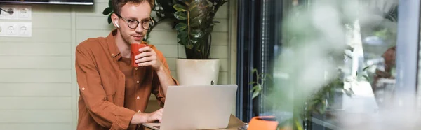 Freelancer em óculos olhando para laptop e segurando copo, banner — Fotografia de Stock