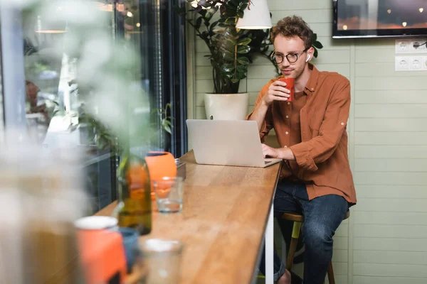 Freelancer in glasses looking at laptop and holding cup — Stock Photo