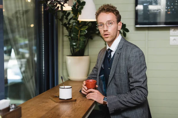 Jovem empresário em uso formal segurando xícara de café no café — Fotografia de Stock