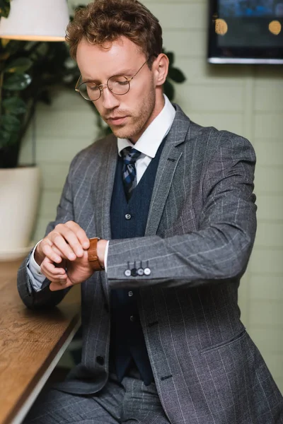 Уверенный бизнесмен в формальной одежде глядя на наручные часы в кафе — стоковое фото