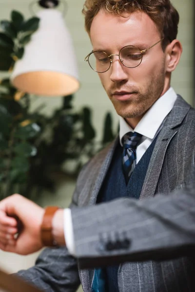 Jovem empresário em desgaste formal olhando para relógio de pulso no café — Fotografia de Stock