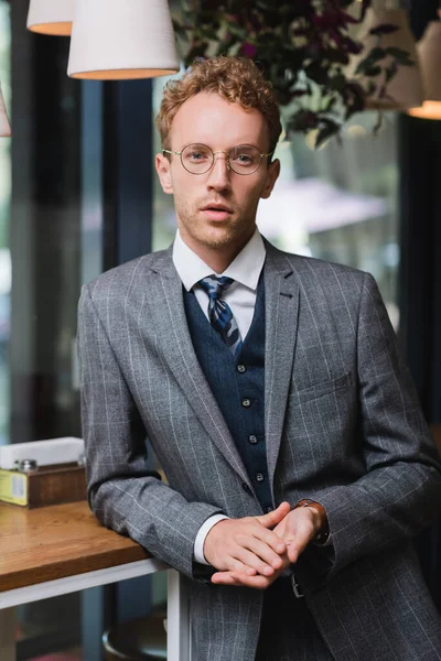 Confiant jeune homme d'affaires en tenue formelle et lunettes regardant la caméra dans le café — Photo de stock