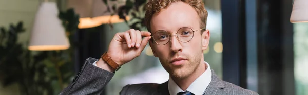 Confident young businessman in formal wear adjusting glasses in cafe, banner — Stock Photo