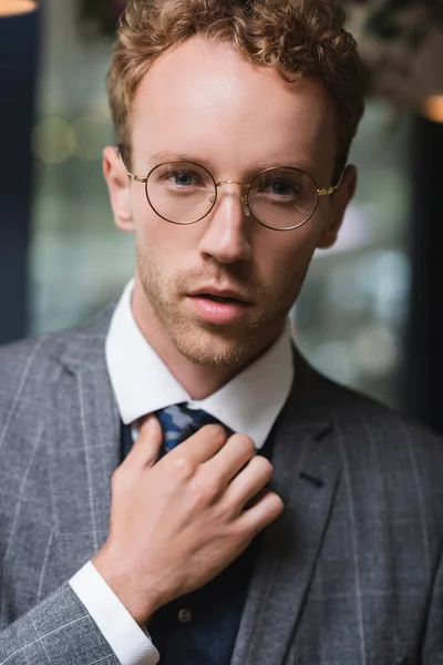 Симпатичный молодой бизнесмен в формальной одежде и очках, регулирующий галстук в кафе — стоковое фото