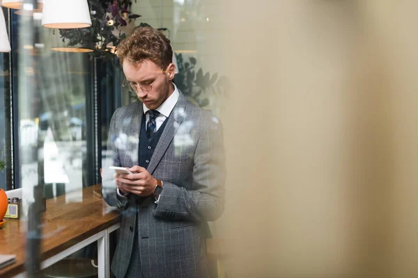 Giovane uomo d'affari in abbigliamento formale messaggistica su smartphone in caffè — Foto stock