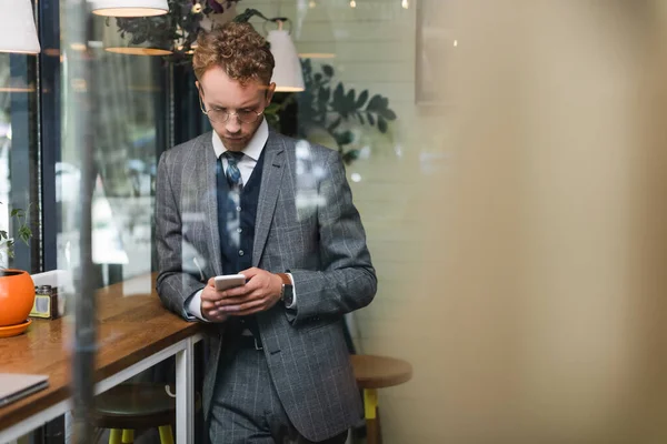 Focado jovem empresário em mensagens formais de desgaste no smartphone no café — Fotografia de Stock