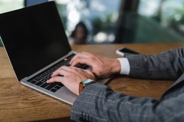 Cropped view of businessman in suit typing on laptop with blank screen in cafe — Stock Photo