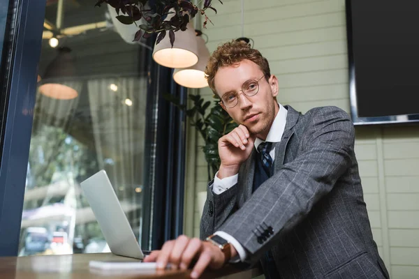 Homme d'affaires en costume atteignant smartphone flou près d'un ordinateur portable dans un café — Photo de stock