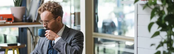 Curly businessman in formal wear and glasses drinking coffee in cafe, banner — Stock Photo