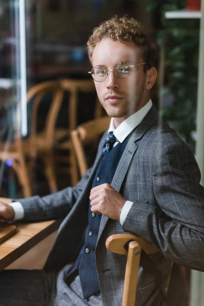Hombre de negocios rizado en gafas mirando a la cámara a través de una ventana borrosa en la cafetería - foto de stock