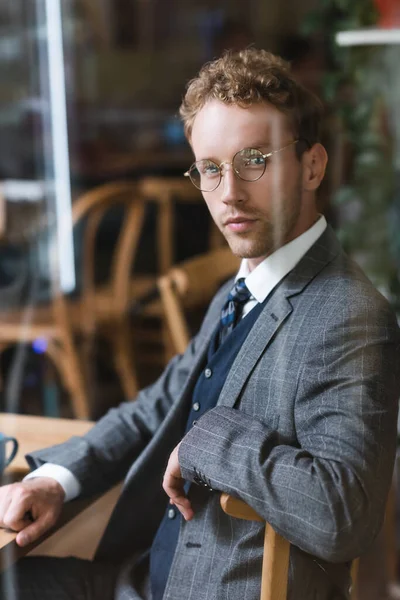 Впевнений бізнесмен в окулярах дивиться на камеру через розмите вікно в кафе — стокове фото