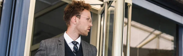 Uomo d'affari riccio in occhiali guardando lontano mentre lascia caffè, banner — Foto stock