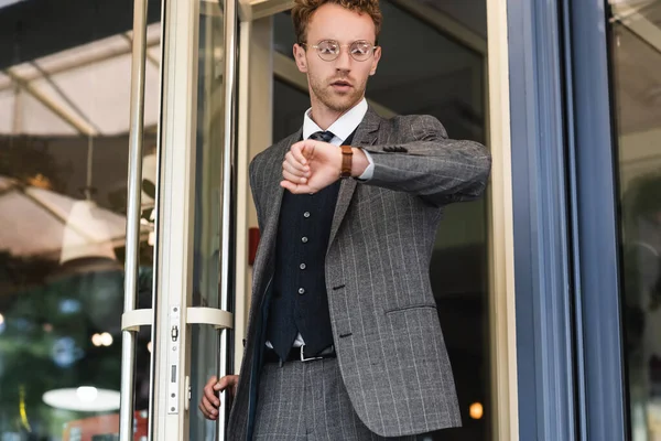 Curly businessman in classy suit looking at wristwatch while leaving cafe — Stock Photo