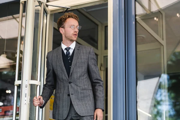 Uomo d'affari riccio in occhiali e vestito di classe porta di apertura lasciando caffè — Foto stock