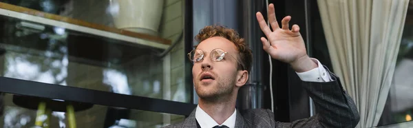 Uomo d'affari in occhiali con mano alzata che chiama il cameriere su terrazza di caffè, stendardo — Foto stock