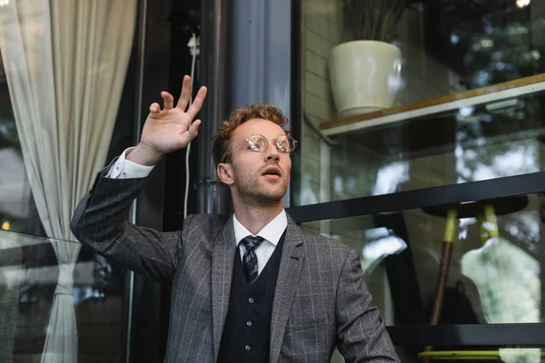 Homem de negócios em copos com mão levantada chamando garçom no terraço do café — Fotografia de Stock