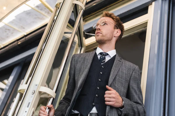 Low angle view of curly businessman in glasses and classy suit opening door while leaving cafe — Stock Photo