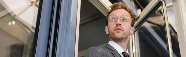 Vista de ángulo bajo del hombre de negocios rizado en gafas que abren la puerta al salir de la cafetería, pancarta - foto de stock