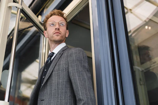 Low angle view of businessman in glasses opening door while leaving cafe — Stock Photo