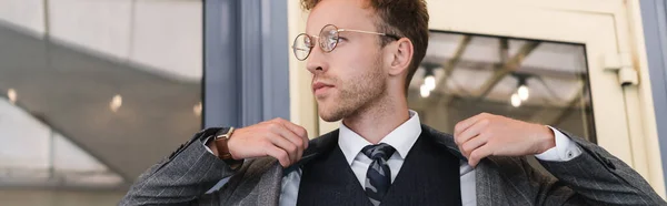Homem de negócios encaracolado em óculos e terno elegante vestindo blazer perto da entrada do café, banner — Fotografia de Stock