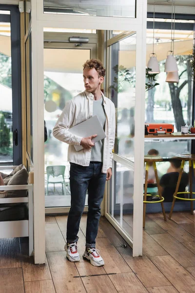 Volle Länge der lockigen Freelancer mit Laptop beim Betreten des Cafés — Stockfoto