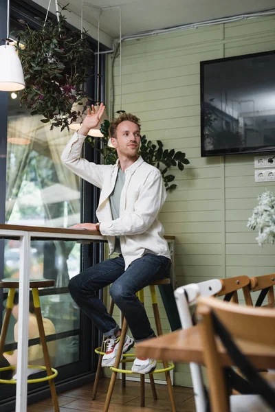 Joyful young man waving hand while calling waiter in cafe — Stock Photo