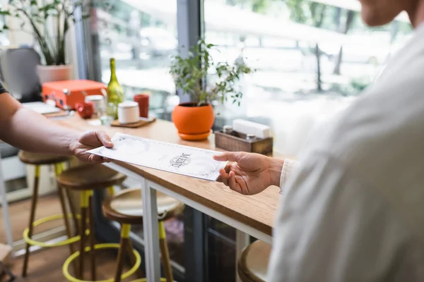 Vista recortada del camarero dando menú al cliente en la cafetería - foto de stock