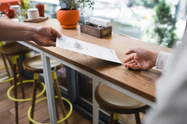 Vista parcial del camarero dando menú al cliente en la cafetería - foto de stock