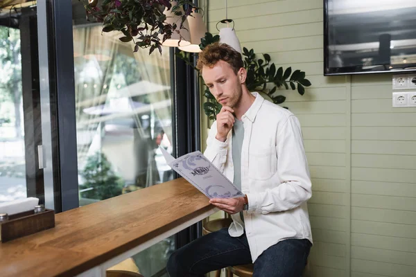 Nachdenklicher junger Mann schaut Speisekarte im Café an — Stockfoto