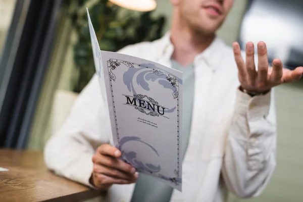 Cropped view of blurred young man holding menu and gesturing in cafe — Stock Photo